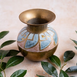 May include: A brass vase with a wide, flared rim and a rounded body. The vase is adorned with a pattern of blue and pink shapes, accented with gold leaf. Green leaves frame the vase.