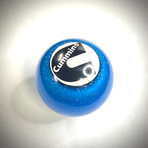 May include: Blue gear shift knob with a white and black Cummins logo.