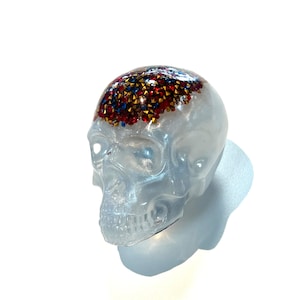 May include: A white resin skull with red, blue, and gold glitter on the top of the head.
