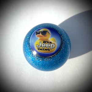 May include: A blue glitter ball with a yellow rubber duck wearing sunglasses and the text "It's a Jeep Thing".
