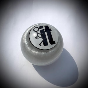 Puede incluir: Una taza de cerámica blanca con un asa negra y el texto "But First, Coffee" en negrita negra. La taza se encuentra sobre un fondo neutro, resaltando su diseño sencillo.
