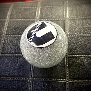 May include: A silver glitter ball with a black and white Cummins logo.