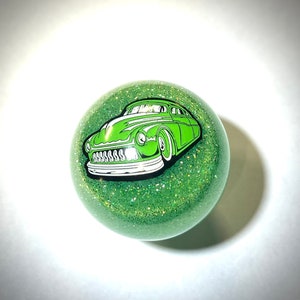 以下が含まれることがあります： 緑色のグリッターの車のシフトノブで、緑色のビンテージカーのグラフィックが描かれています。