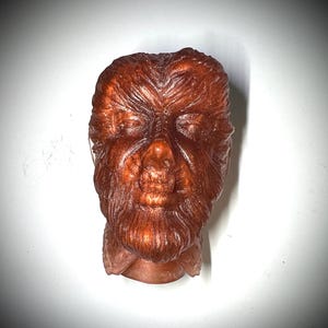 以下が含まれることがあります： 茶色の狼男の頭部の彫刻のクローズアップ。彫刻は樹脂のような素材で作られており、詳細なテクスチャのある表面をしています。