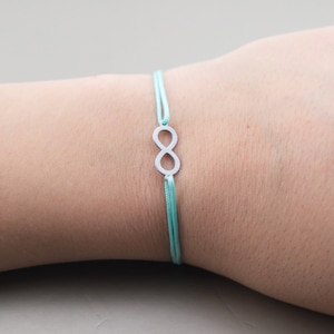 Può includere: Un braccialetto di corda blu chiaro con un ciondolo a forma di infinito in argento.