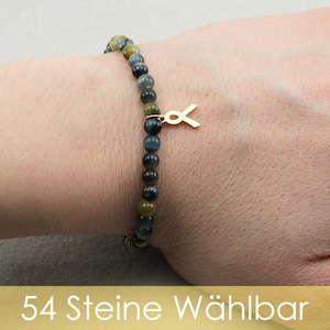 Könnte beinhalten: Ein Perlenarmband mit kleinen, runden, polierten Steinen in Blau-, Grau- und Goldtönen. Das Armband enthält einen kleinen, goldfarbenen Metallanhänger in Form einer Schleife. Der Text 54 Steine Wählbar ist am unteren Bildrand zu sehen.