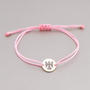Può includere: Un braccialetto di corda rosa con un ciondolo dorato con un design di angelo ritagliato.