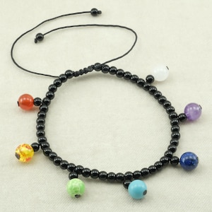 Può includere: Bracciale con perline nere con accenti di pietre preziose colorate. Il bracciale presenta una serie di piccole perline nere rotonde con pietre preziose rotonde più grandi in rosso, giallo, verde, blu, viola e bianco. Ha un cordino nero regolabile.