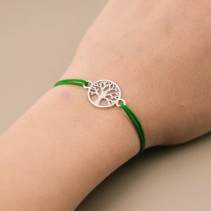 Pode incluir: Um bracelete de corda verde com um fecho de prata em forma de árvore da vida.