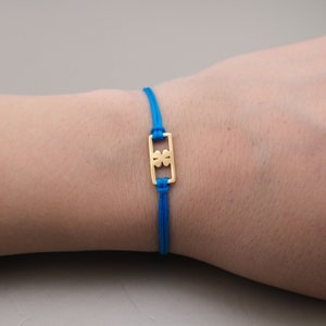 May include: A blue string bracelet with a gold charm featuring a four-leaf clover design.