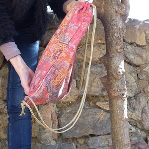 May include: A red and gold drawstring bag with a patterned design. The bag is made of fabric and has a long gold chain strap.