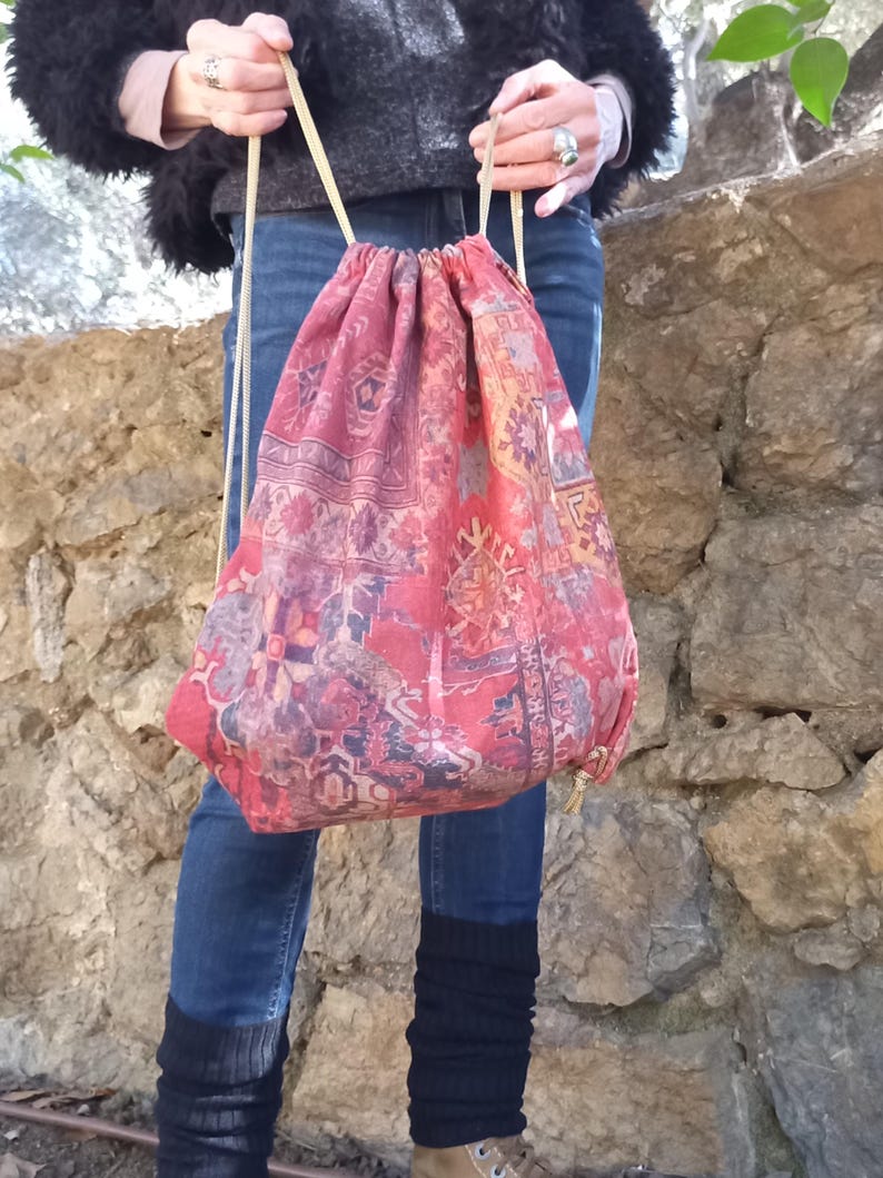 May include: A red drawstring bag with a colorful patterned design. The bag is made of fabric and has a long drawstring.