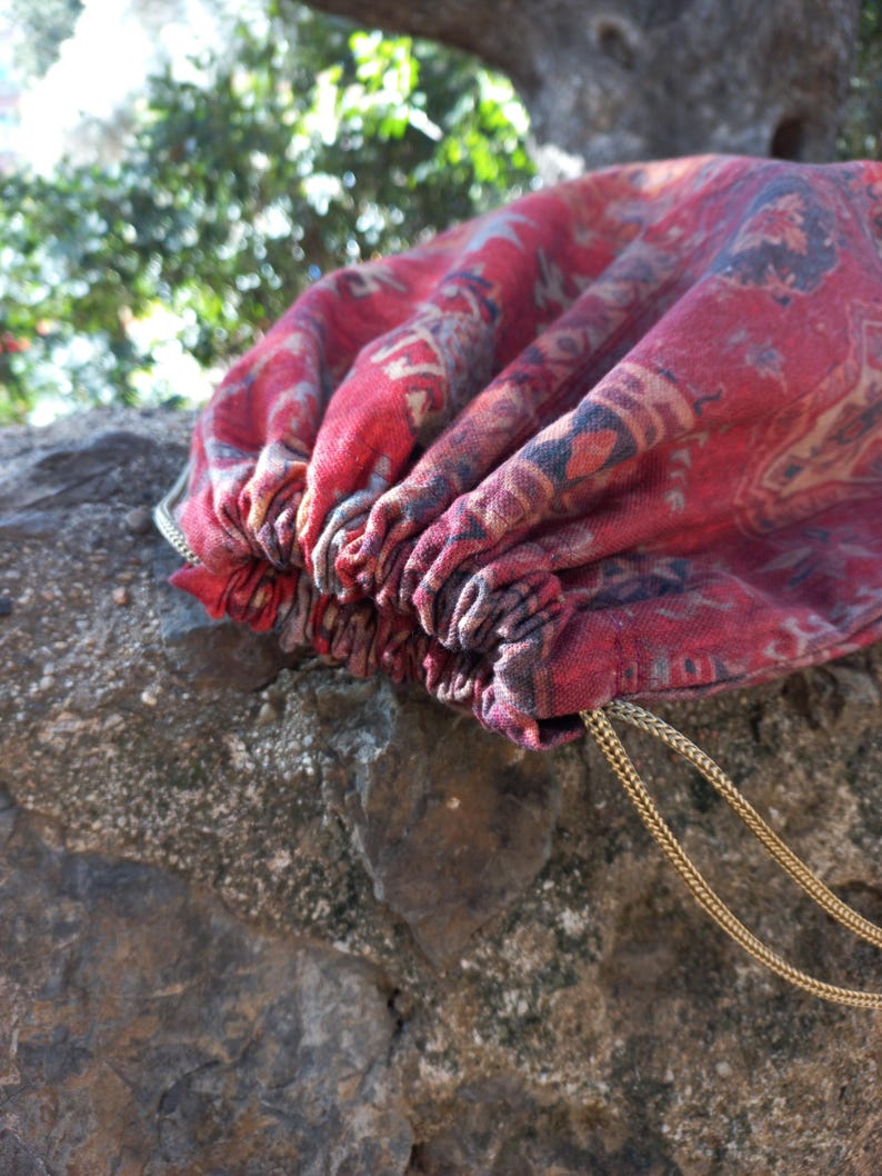 May include: A red and blue patterned drawstring bag with gold cords. The bag is made of fabric and has a gathered top.