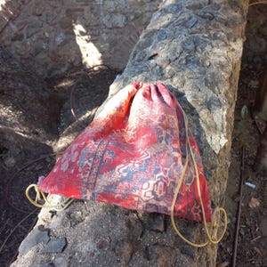May include: A red and blue drawstring bag with a patterned design. The bag is made of fabric and has a gold drawstring.