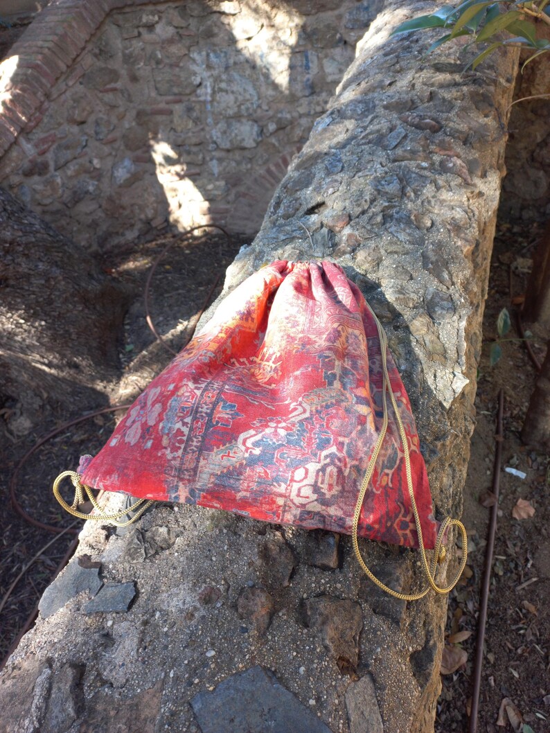 May include: A red and blue drawstring bag with a patterned design. The bag is made of fabric and has a gold drawstring.