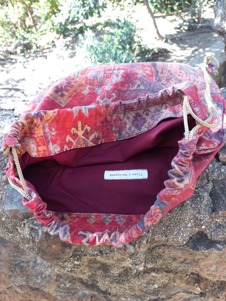 May include: Red drawstring bag with a patterned fabric design. The bag is lined with a burgundy fabric and has a white label that reads "Tilda & Matilda".