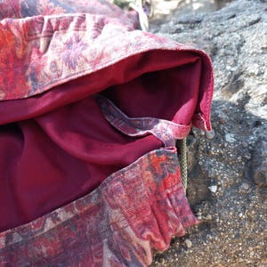 May include: A close-up of a red and beige patterned fabric with a burgundy lining. The fabric is folded over and the lining is visible. The fabric is textured and has a subtle sheen.