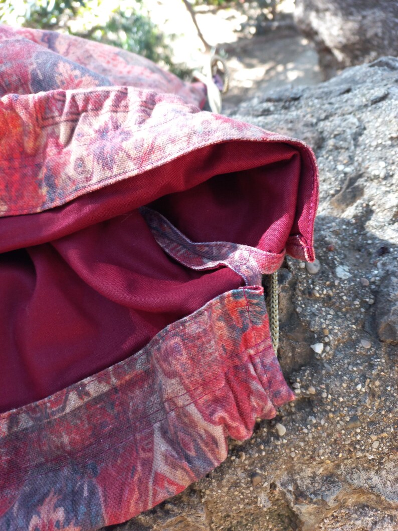 May include: A close-up of a red and beige patterned fabric with a burgundy lining. The fabric is folded over and the lining is visible. The fabric is textured and has a subtle sheen.