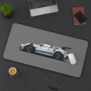 May include: A gray mousepad featuring a white sports car illustration with black accents and the text "GT3 RS". A white computer mouse is next to the car. The mousepad is on a dark gray surface.