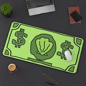 Könnte beinhalten: Eine grüne Mausunterlage mit einem Dollar-Schein-Design. Die Mausunterlage zeigt zwei Dollarzeichen und eine zentrale Illustration einer Muschel. Eine weiße Maus liegt auf dem Pad, mit einem Laptop, einem Notizbuch und einer Kaffeetasse in der Nähe.