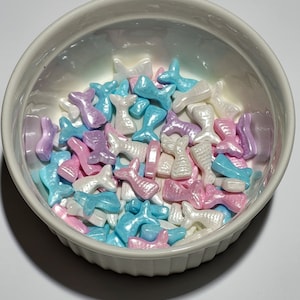 Può includere: Una ciotola bianca piena di code di sirena di zucchero color pastello. Le code di sirena sono in tonalità di rosa, blu e bianco.