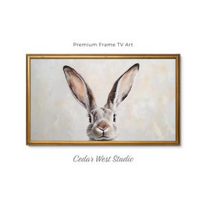 May include: A rectangular wall art piece featuring a painting of a rabbit with long ears, set in a gold-toned frame. The artwork displays the text Premium Frame TV Art and Cedar West Studio. The rabbit is rendered in shades of brown, white, and gray.