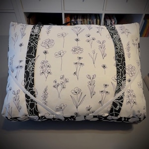 May include: Rectangular cushion with a white base and black floral line drawings. The cushion has black patterned side panels and white piping. The design features various floral illustrations, creating a botanical theme.