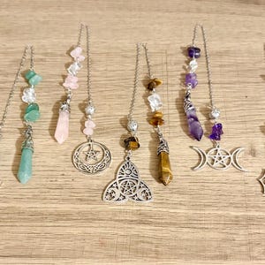 May include: Five silver-toned metal chains featuring assorted gemstone beads and charms. The charms include a lotus flower, a pentacle within a crescent moon, a triquetra with a pentacle, a triple moon symbol, and a seated figure in a circle.