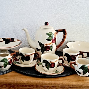 May include: A vintage tea set with a brown and green floral pattern. The set includes a teapot, creamer, sugar bowl, four cups and saucers, and a serving bowl.