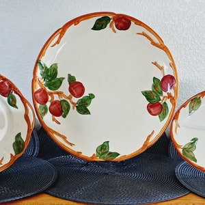 Puede incluir: Tres fuentes de cerámica blanca con diseño de frutas. Las fuentes presentan un patrón de manzanas rojas y hojas verdes con ramas marrones en los bordes. Las fuentes son ovaladas, redondas y festoneadas.