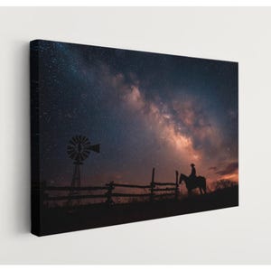 May include: Canvas print featuring a silhouette of a cowboy on horseback against a backdrop of a starry night sky. A windmill and wooden fence are also silhouetted in the foreground. The sky transitions from dark blue to orange.