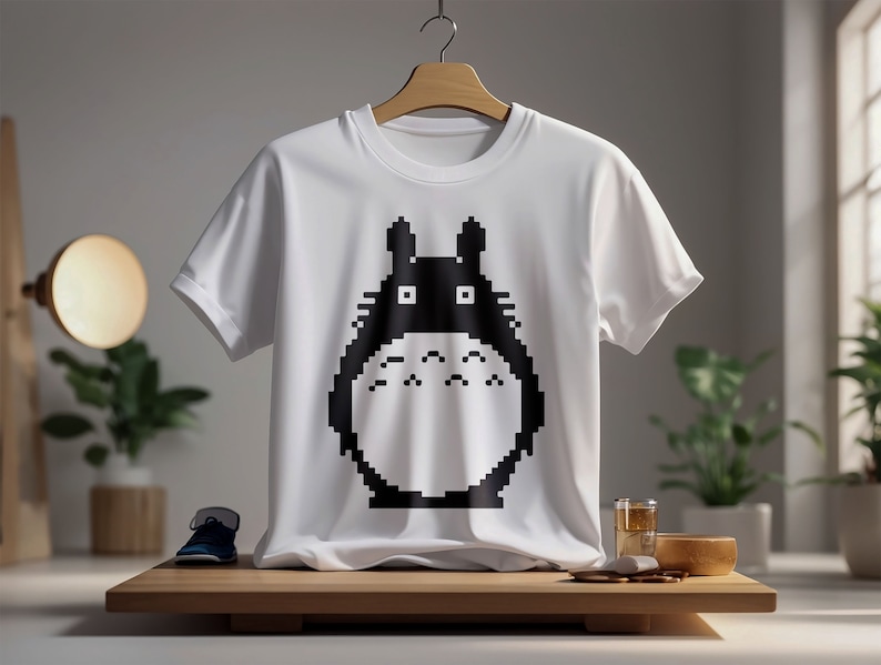 May include: White t-shirt with a black pixelated graphic of Totoro from the movie My Neighbor Totoro.