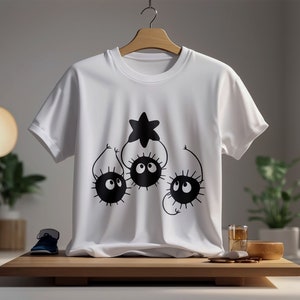 May include: White t-shirt with a black graphic of three cartoon characters with large eyes and spiky bodies reaching up to a star.