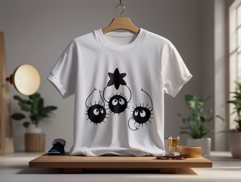 May include: White t-shirt with a black graphic of three cartoon characters with large eyes and spiky bodies reaching up to a star.