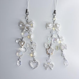 Peut inclure: Deux breloques de téléphone blanches avec un nœud blanc, des perles de perles et d'autres breloques décoratives.