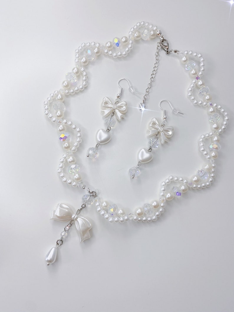 A white pearl twirl necklace with iridescent beads and pearl bows with in the middle matching earrings with a pearl bow, iridescent beads and pearl hearts.