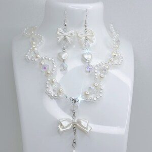 A white pearl twirl necklace with iridescent beads and pearl bows with in the middle matching earrings with a pearl bow, iridescent beads and pearl hearts.
