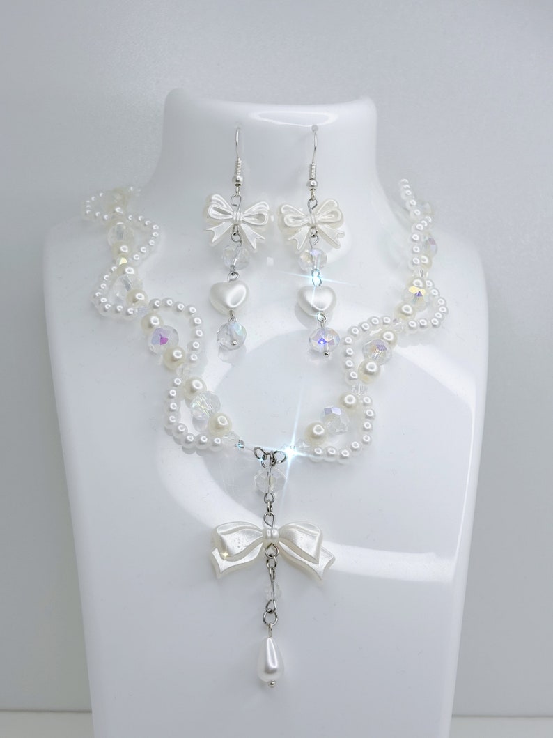 A white pearl twirl necklace with iridescent beads and pearl bows with in the middle matching earrings with a pearl bow, iridescent beads and pearl hearts.