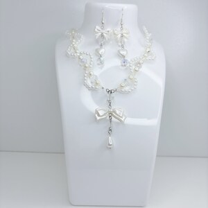 A white pearl twirl necklace with iridescent beads and pearl bows with in the middle matching earrings with a pearl bow, iridescent beads and pearl hearts.