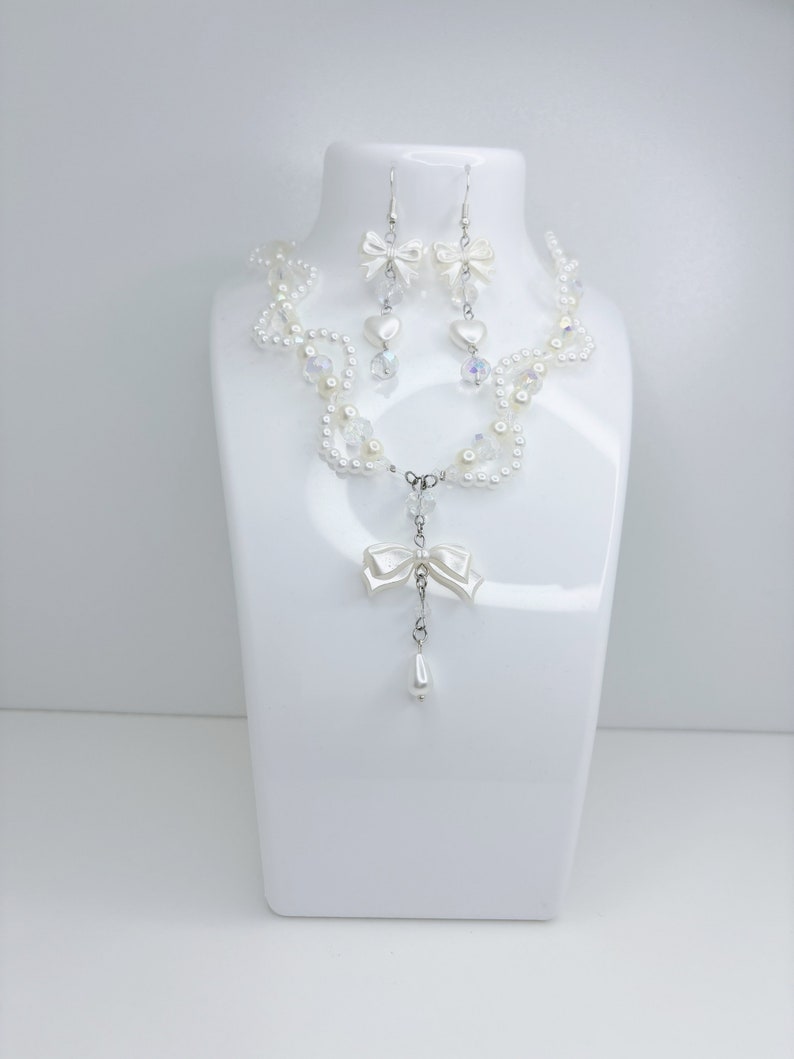 A white pearl twirl necklace with iridescent beads and pearl bows with in the middle matching earrings with a pearl bow, iridescent beads and pearl hearts.