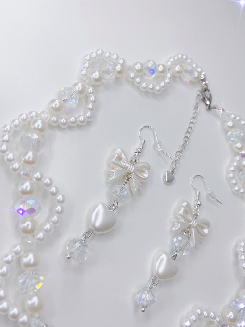A white pearl twirl necklace with iridescent beads and pearl bows with in the middle matching earrings with a pearl bow, iridescent beads and pearl hearts.