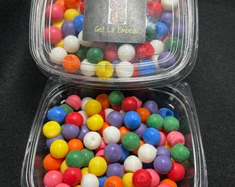 May include: A clear plastic container filled with 100 colorful gumballs. The container has a label that reads "100 Gumballs Get Lit Embeds".