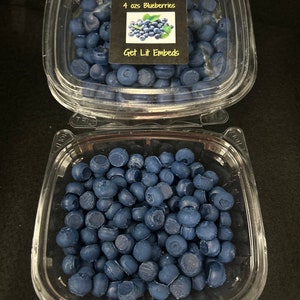 Peut inclure: Deux récipients en plastique transparent remplis de petites billes de cire bleu mat en forme de myrtilles. Le récipient supérieur porte une étiquette carrée noire avec le texte 4 ozs Blueberries et Get Lit Embeds, ainsi qu'une image de myrtilles.
