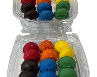 May include: Two clear plastic containers filled with colorful candies. Each container holds a variety of candies in red, orange, yellow, green, blue, and brown. The candies have a rounded shape and a letter "M" printed on them.