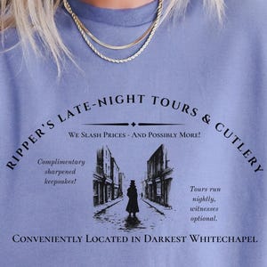 May include: A light blue t-shirt with a black graphic design that says "Ripper's Late-Night Tours & Cutlery" with the text "We Slash Prices - And Possibly More!" underneath. The graphic also includes a black and white illustration of a street scene with a figure in the middle.