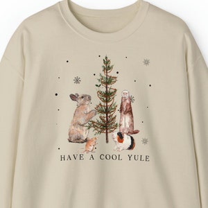 May include: A beige sweatshirt with a Christmas tree and animals decorating it. The text "HAVE A COOL YULE" is printed below the tree.