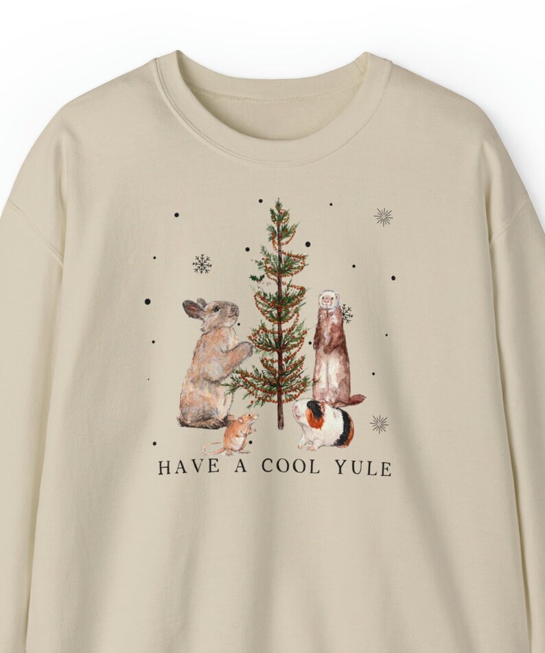 May include: A beige sweatshirt with a Christmas tree and animals decorating it. The text "HAVE A COOL YULE" is printed below the tree.