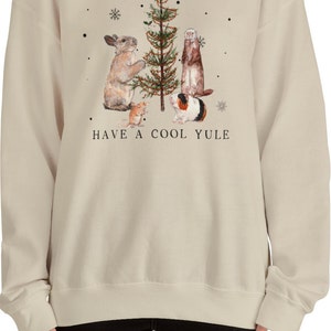 May include: A beige sweatshirt with a Christmas tree and animals decorating it. The text "HAVE A COOL YULE" is printed below the image.