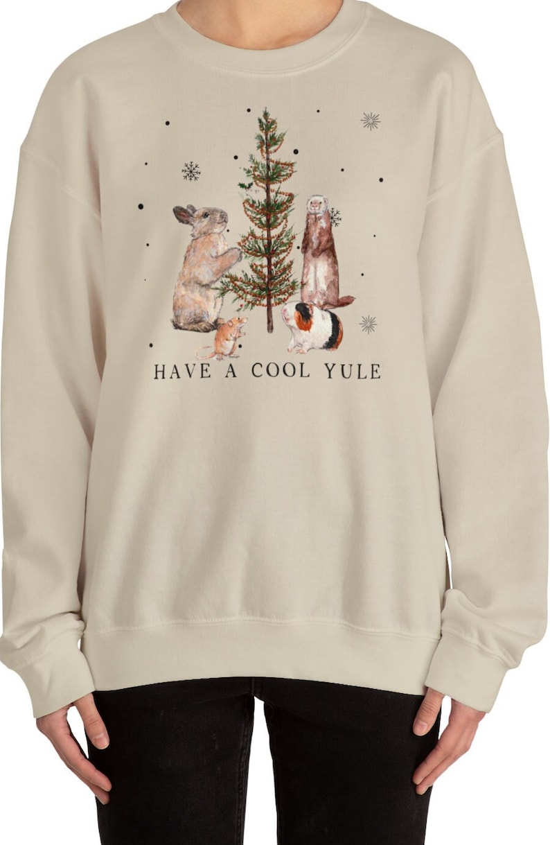 May include: A beige sweatshirt with a Christmas tree and animals decorating it. The text "HAVE A COOL YULE" is printed below the image.