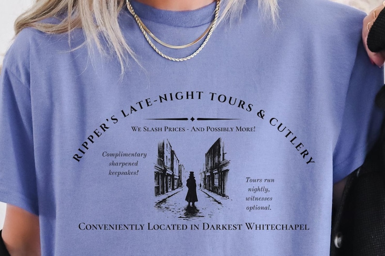 May include: A light blue t-shirt with a black graphic design that says "Ripper's Late-Night Tours & Cutlery" with the text "We Slash Prices - And Possibly More!" underneath. The graphic also includes a black and white illustration of a street scene with a figure in the middle.